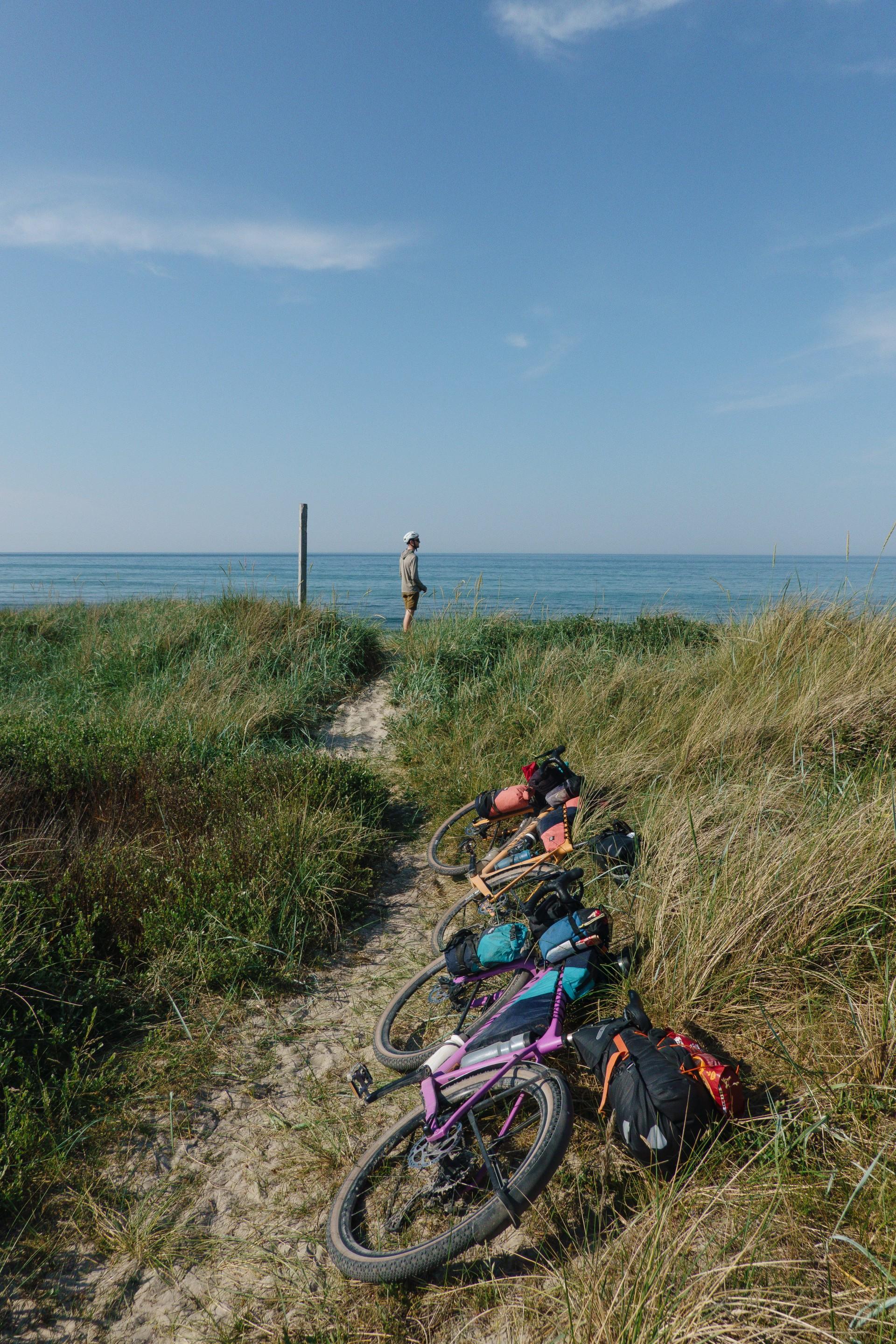 A satisfied Hannes, our creator, having laid down his bike with custom bike bags after a long day of riding, looking out over sandy dunes and the ocean in the distance.